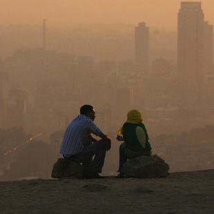 An Egyptian couple chat at the top of a mountain area that looks over Cairo during a smoggy day