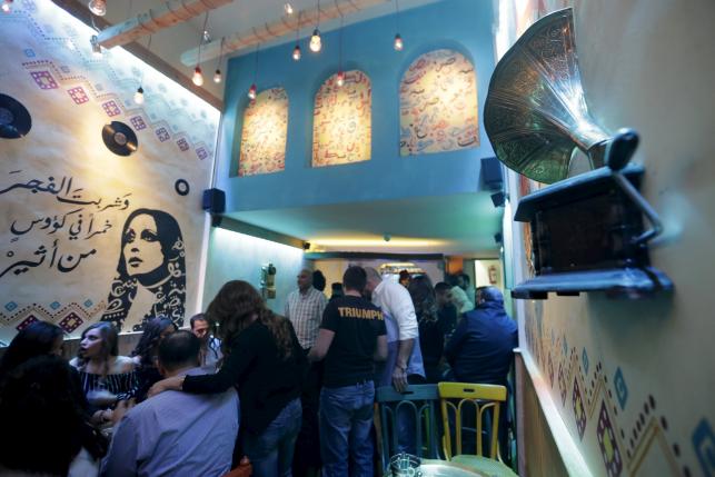 People sit at a newly opened pub near a stencil of Lebanese singer Fayrouz in Damascus, Syria.